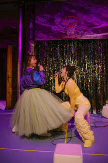 Die Schauspielerinnen Coco Brell und Mara Romei stehen in bunten Klamotten auf der Bühne