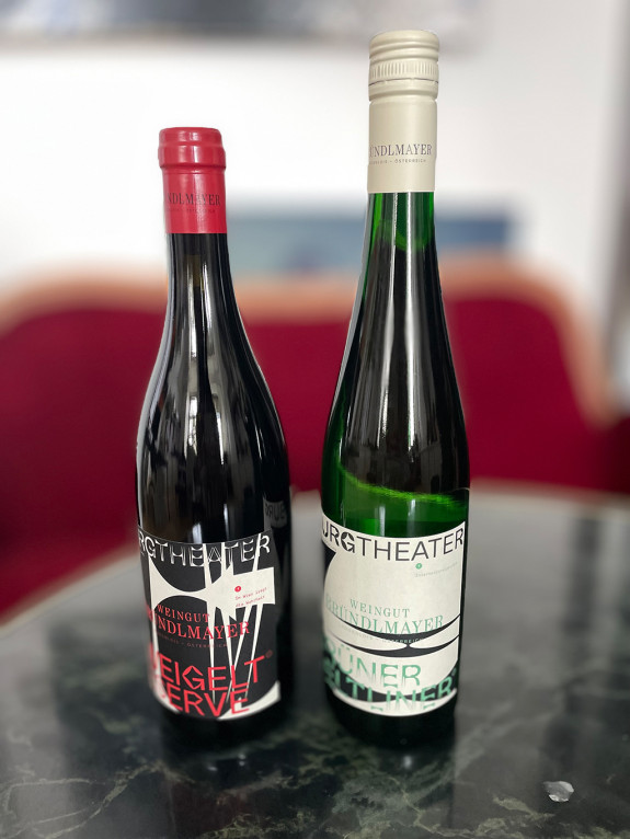 Zwei volle Weinflaschen, eine mit roten und einem mit hellem Etikett, stehen auf einem Tisch