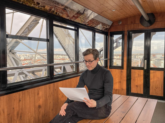 Markus Meyer sitz alleine in einer Kabine des Wiener Riesenrads mit Blick über die Stadt und liest auf einem Blatt Papier