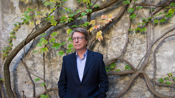 Portraitbild des Autors Peter Rosei vor einer mit Pflanzen bewachsenen grauen Hauswand 